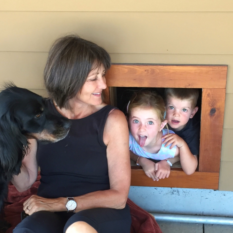 Children peek out of doghouse as Grandma and dog look on